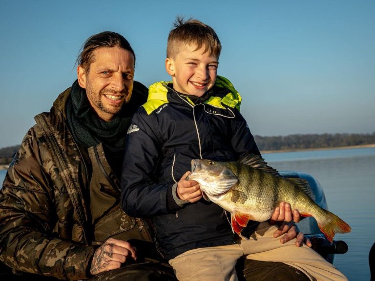 Baars Vader en zoon tonen trots hun gevangen baars aan het water.