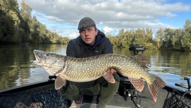 Visgids Dutch Fishing Experience Man houdt grote snoek vast op een boot, met een waterachtige achtergrond.