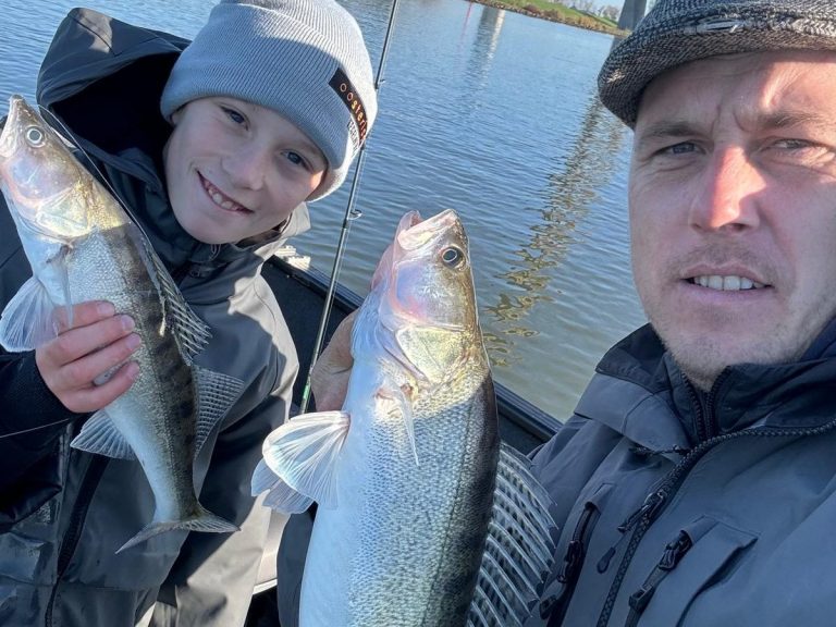 Visgids Dutch Fishing Experience Een man en een jongen tonen trots hun gevangen vissen langs een waterweg.
